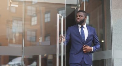 Handsome confident african businessman in formal suit walking out of modern office center